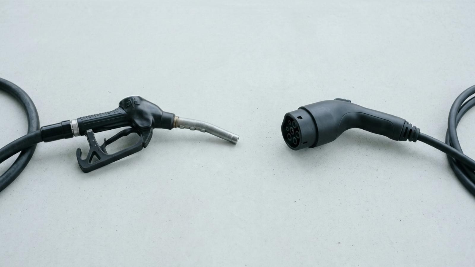 A petrol pump nozzle and an EV charging connector facing each other on a pale background